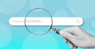 A hand holding a magnifying glass over a search bar that says 'Keyword Research...' on a soft blue background